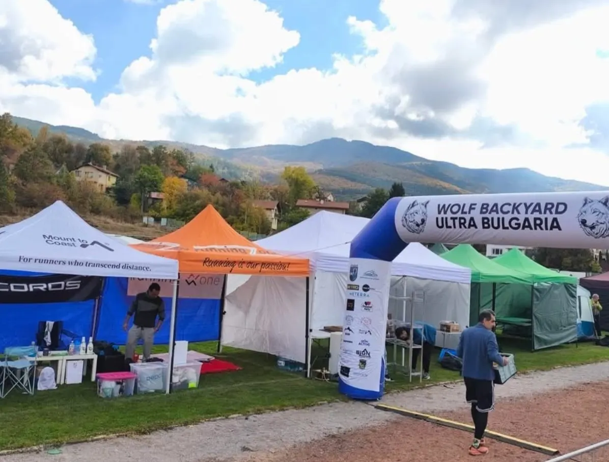 Event tents, including a COROS tent, next to the Wolf Backyard Ultra Bulgaria start arch at the stadium in Vladaya