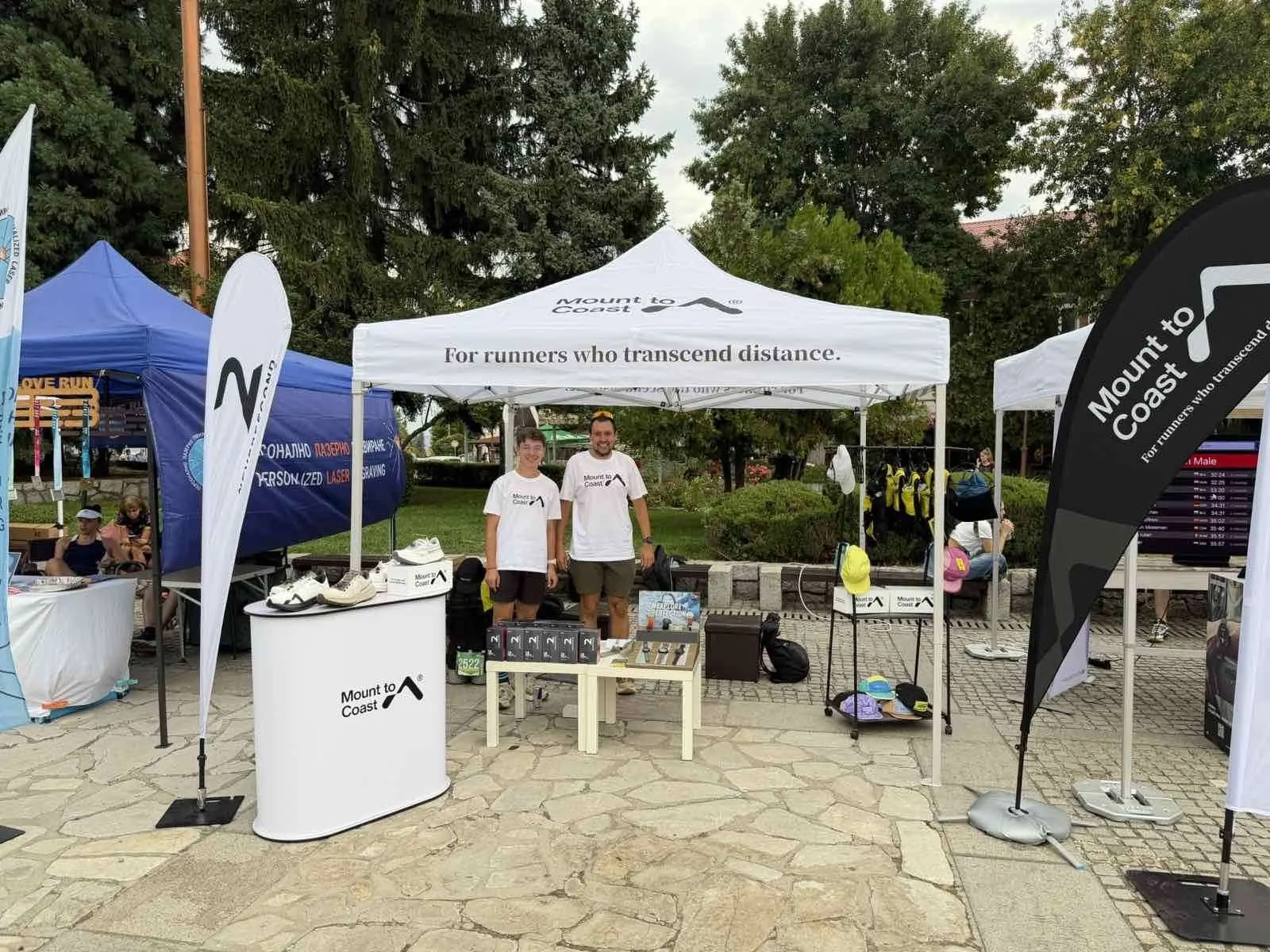 Mount to Coast expo tent at Pirin Ultra with two team members; Neversecond flag beside the tent